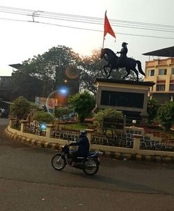 Man riding bicycle on street against sky in city