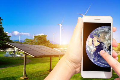 Cropped hand using phone with globe on screen by solar panels 