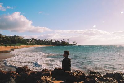 Rear view of man sitting on rock at beach