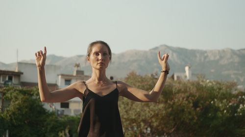 Young woman with arms raised standing against trees