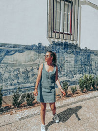 Full length of young woman standing against building in city