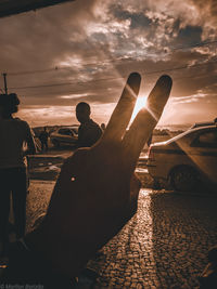 Cropped hand gesturing peace sign against sunny sky during sunset