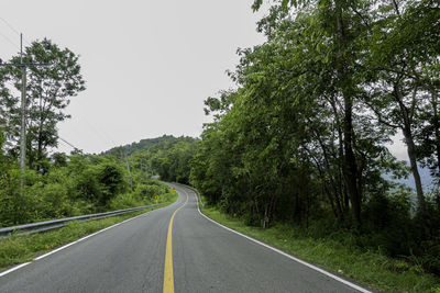 Empty road amidst trees against clear sky