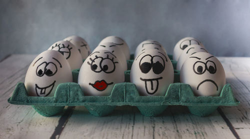 Close-up of anthropomorphic faced eggs on tray at table against wall