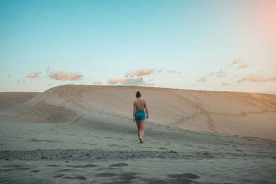 Rear view of woman standing at beach against sky