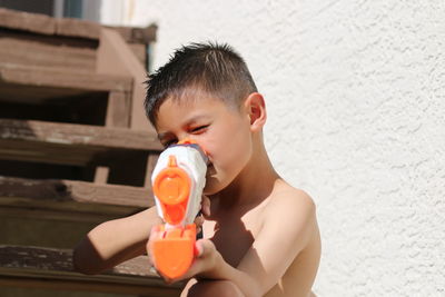 Portrait of shirtless boy with squirt gun on wooden steps