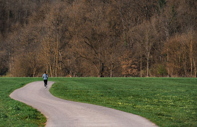 Rear view full length of woman jogging amidst field on road