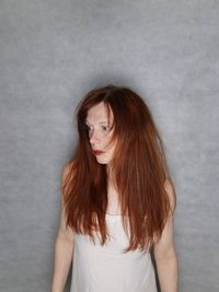 Portrait of young woman standing against wall red hair