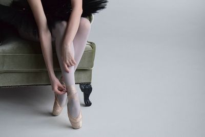Low section of ballet dancer wearing shoe while sitting on sofa