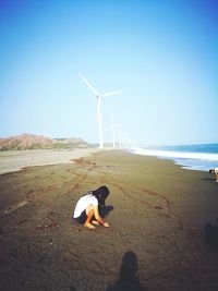 Side view of woman crouching against windmills at beach