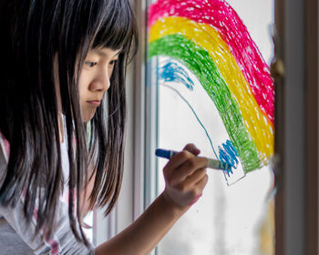 Close-up of girl coloring on window at home