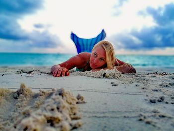 Woman lying down on beach against sky