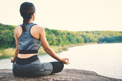 Rear view of woman doing yoga by lake