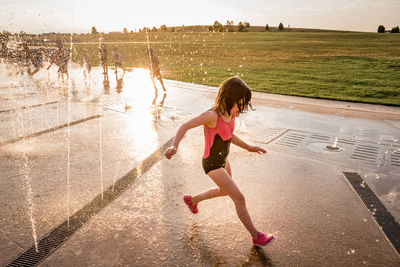 Young girl in bathing suit runs through splash pad of squirting water