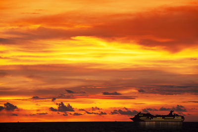 Silhouette cruise ship sailing on sea against cloudy sky at sunrise