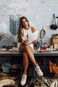Fashion designer holding paper and tablet pc sitting on workbench