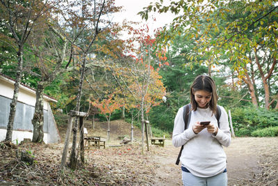 Woman using phone while standing against trees