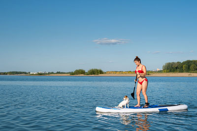 Dog swims on the board with the owner. a woman and her pet spend time together at the lake