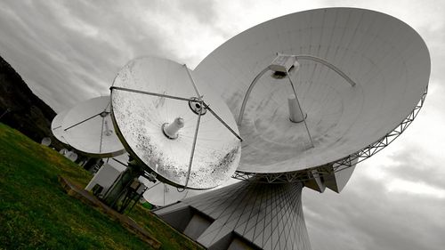 Low angle view of satellite dishes against cloudy sky