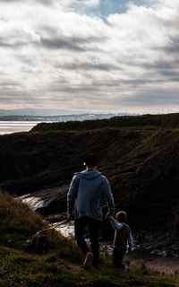 Rear view of father and son walking on mountain against cloudy sky during sunset