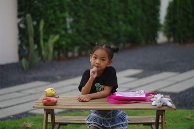 Portrait of girl with spoon in mouth sitting on bench