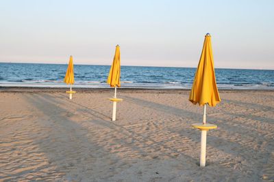 Closed parasols at beach against sky