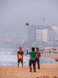 Full length of men playing on beach against sky in city