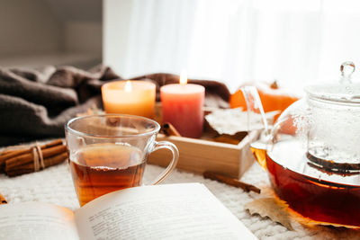 Autumn mood, a burning candle, a book and a kettle of hot tea on a cozy plaid. atmospheric