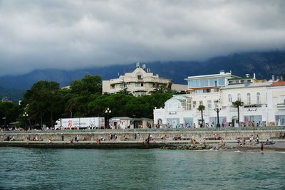 View of town at waterfront against cloudy sky