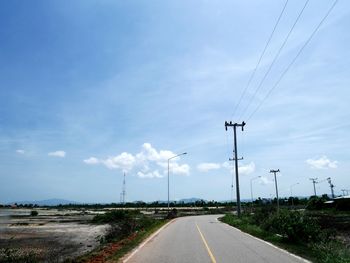 Road by electricity pylon against sky