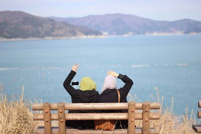 Rear view of men sitting on mountain by sea