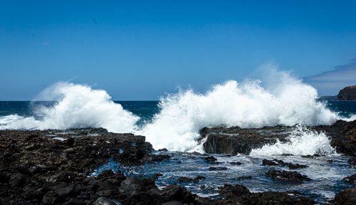 Waves splashing on rocks against clear sky