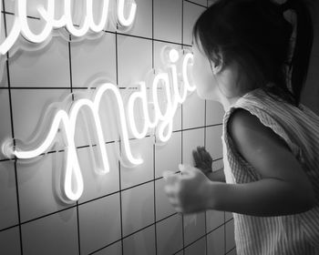 Side view of girl looking at illuminated text on wall