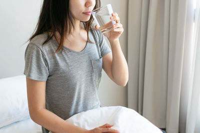 Young woman drinking milk while sitting on bed at home