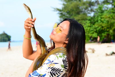 Young woman holding snake while standing at beach