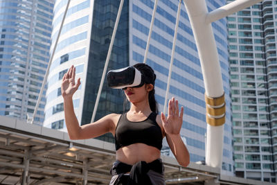 Woman wearing 3-d glasses while gesturing against building