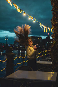 Young woman with tousled hair holding illuminated string light at night