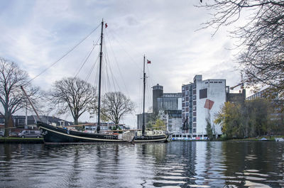 Sailboats moored on river by buildings in city against sky