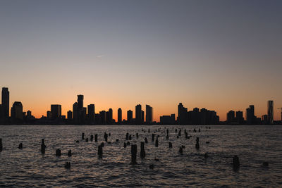 Silhouette buildings by sea against clear sky during sunset