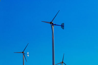 Low angle view of wind turbines against clear blue sky