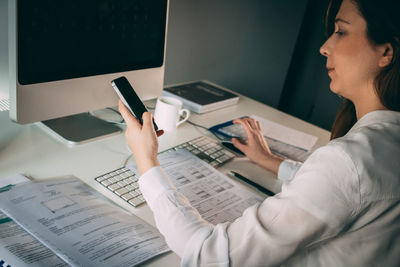 Businesswoman using smart phone while working on table