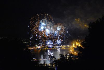 Firework display over illuminated city against sky at night