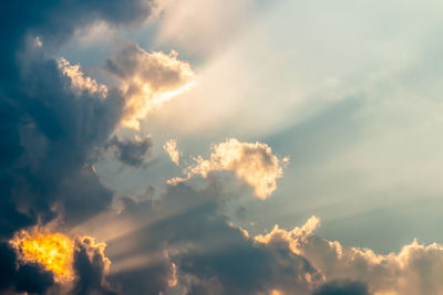 Low angle view of sunlight streaming through clouds