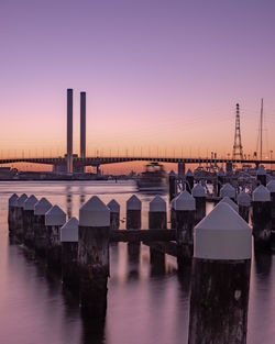 Bridge over river by buildings against sky at sunset