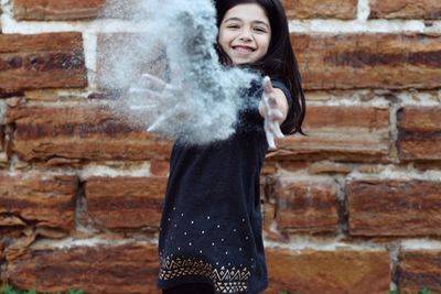 Portrait of young woman standing against brick wall