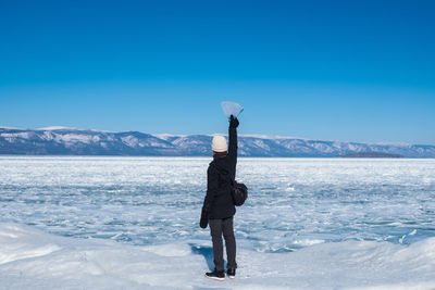 Woman standing on snowcapped mountain against blue sky