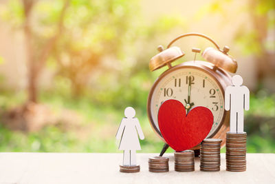 Close-up of figurines with stacked coins and alarm clock on table