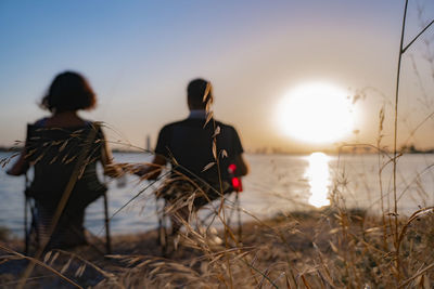 Rear view of people sitting at beach during sunset