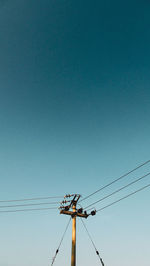 Low angle view of electricity pylon against clear blue sky