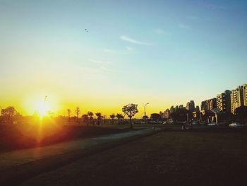 Road by buildings against sky during sunset